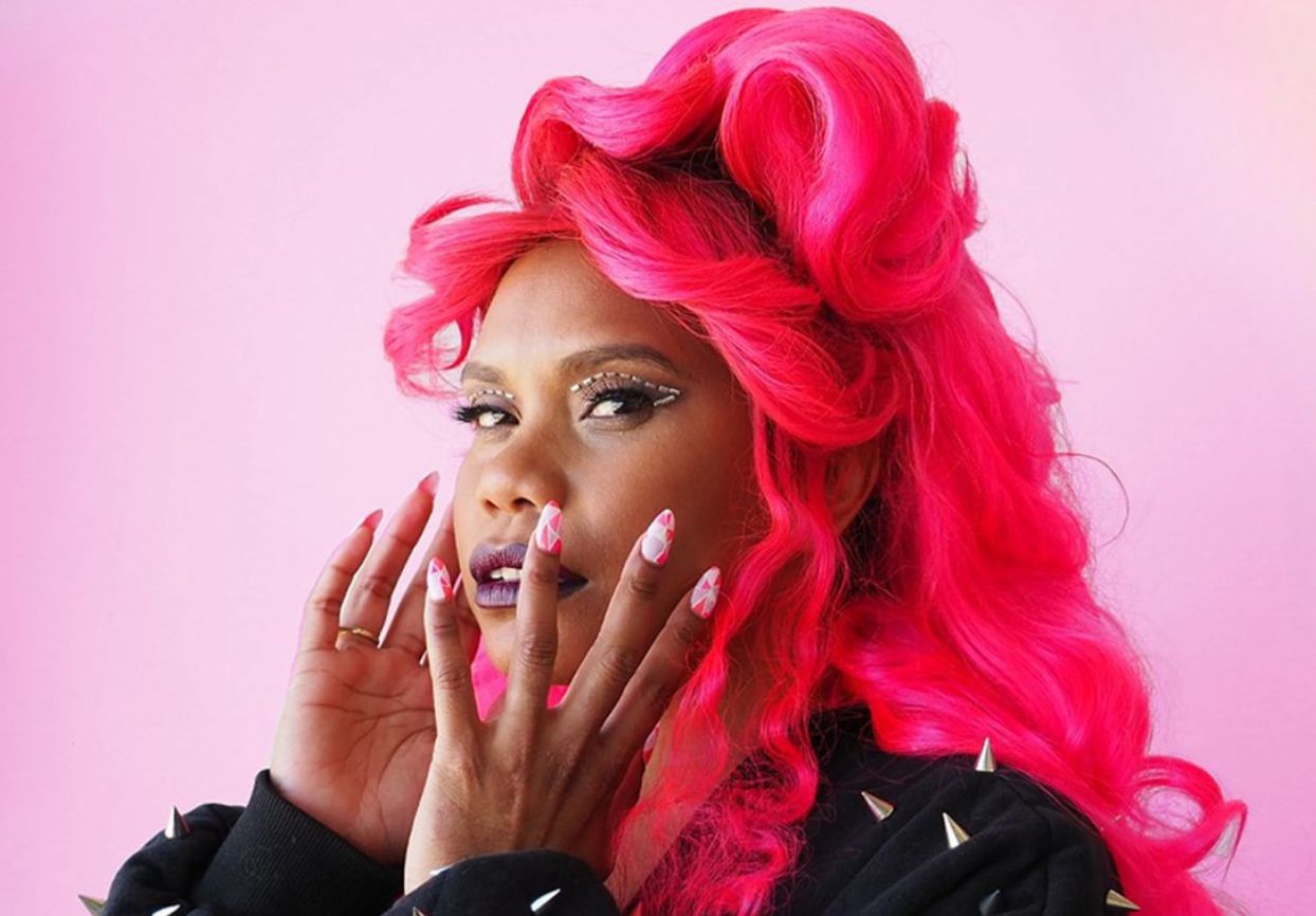 Person with bright pink hair and nail art against a pink background.
