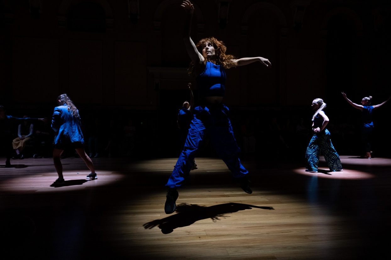 Contemporary dancers dressed in blue, performing under spotlights