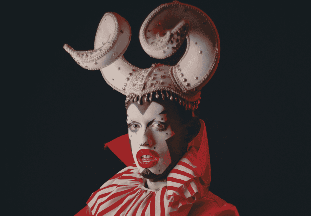 Person in theatrical black and white makeup with a red lip and red outfit, wearing white horns on their head