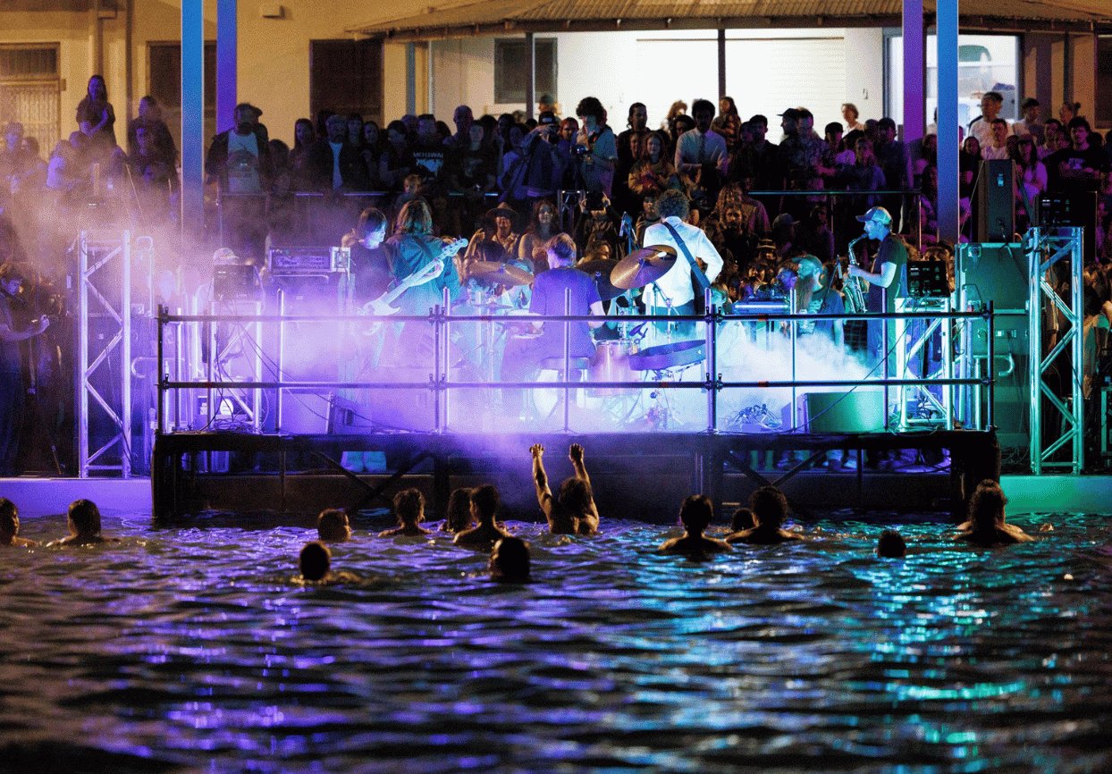 Swimmers in the ocean baths watching a band play at SOAK while a crowd watches on land